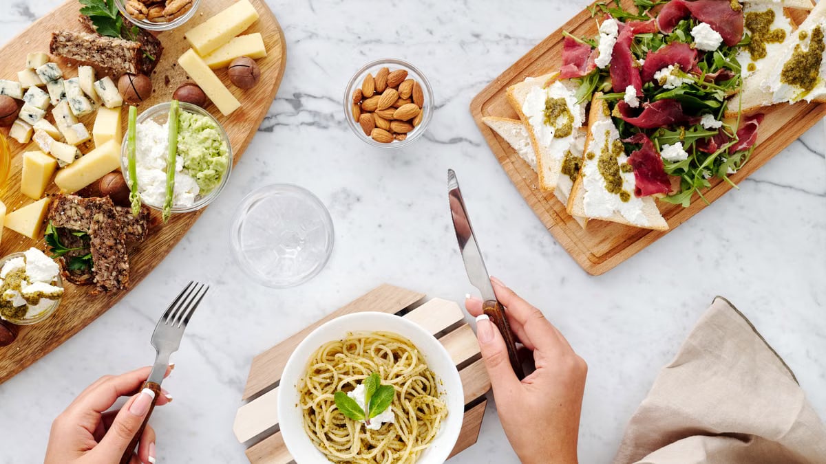 Gourmet table setup featuring cheese, pasta, and appetizers on a marble surface from a top view.